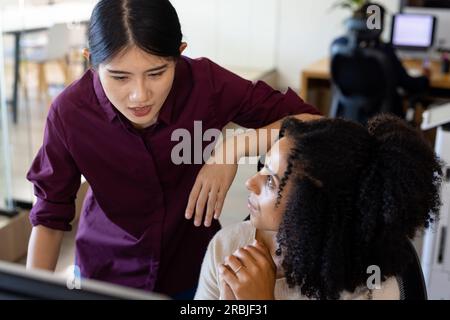 Zwei verschiedene weibliche Geschäftskollegen, die Computer verwenden und über die Arbeit am Schreibtisch im Büro sprechen. Teamarbeit, Arbeit, Geschäft, Kommunikation und zwanglos Stockfoto
