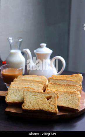 Teezeit-Snack. Gesunder Weizenrusk serviert mit indischem heißen Masala-Tee und Milchkännchen auf schwarzem Hintergrund. Auch bekannt als Mumbai Cutting Chai. Stockfoto