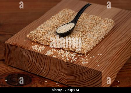 Honigriegel mit Sesamsamen aus der Nahaufnahme auf Holzhintergrund. Gozinaki-Süßigkeiten. Traditionelle orientalische Konfektion mit gerösteten karamellisierten Nüssen. Sesam siehst du Stockfoto