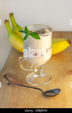 Joghurt Jelly Dessert mit Banane, Erdbeere, Kakao, frischer Minze in einem Glas auf Holzbrett.gesunde hausgemachte süße vegane Speisen.Vanille-Agar-Agar mil Stockfoto