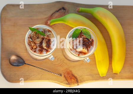 Joghurt Jelly Dessert mit Banane, Erdbeere, Kakao, frischer Minze in einem Glas auf Holzbrett.gesunde vegane süße hausgemachte Speisen.Vanille-Agar-Agar mil Stockfoto