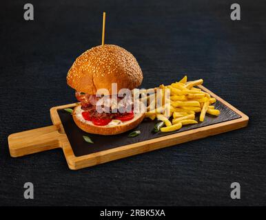 Leckere Burger mit Pommes Frites, serviert auf Schieferbrett Stockfoto