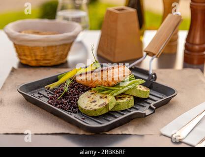 Gebratenes Fischfilet mit wildem Reis und gegrillter Zucchini auf dem Restauranttisch Stockfoto