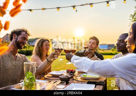 Familie und multiethnische, vielfältige Freunde treffen sich an einem Gartentisch. Leute essen gegrilltes und frisches Gemüse, teilen leckere Salate für eine große Familienfeier mit Verwandten. Hochwertiges Foto Stockfoto