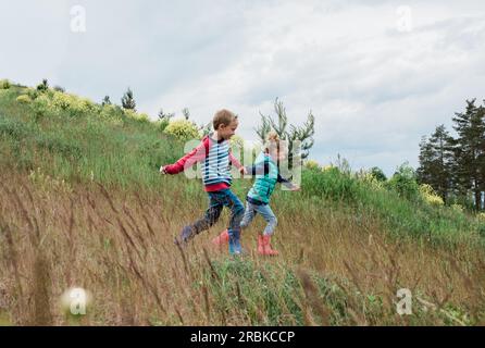 Ein Mädchen und ein Junge, die einen Hügel hinunterlaufen und Händchen halten Stockfoto