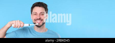 Glücklicher Mann mit elektrischer Zahnbürste auf hellblauem Hintergrund. Bannerdesign mit Platz für Text Stockfoto