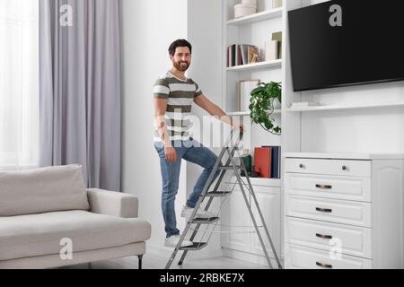 Ein glücklicher Mann auf einer Klappleiter aus Metall zu Hause Stockfoto