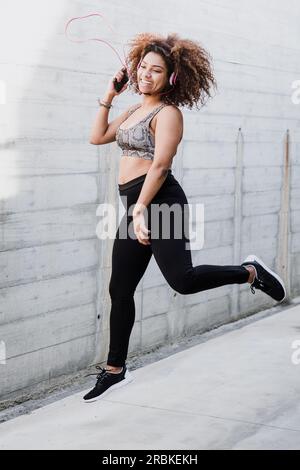 Fröhliche, kurvige afroamerikanische Frau, die hüpft und Musik hört Stockfoto