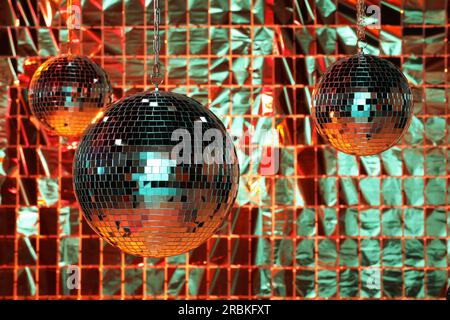 Glänzende Disco-Bälle gegen einen Partyvorhang unter farbigen Lichtern Stockfoto