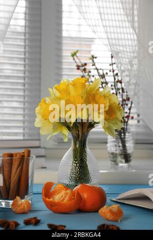 Wunderschöne gelbe Narzissen in Vase, Mandarinen und Zimt auf hellblauem Tisch Stockfoto