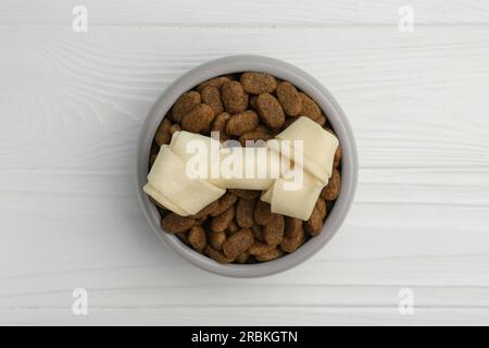 Trockenes Hundefutter und Leckerbissen (geknüpfter Kauknochen) auf weißem Holzboden, Draufsicht Stockfoto