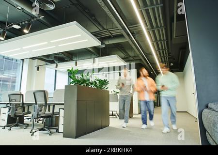 Eine Gruppe kreativer Geschäftspartner, die in einem modernen und geräumigen Gemeinschaftsraum mit High-Tech-Interieur, zeitgenössischen Möbeln und grünen Naturfarben spazieren gehen Stockfoto