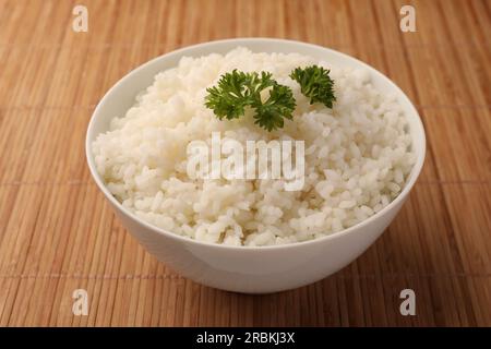 Schüssel mit köstlichem Reis und Petersilie auf Bambusmatte Stockfoto