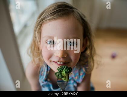 Porträt eines jungen Mädchens mit einem schmutzigen Gesicht, das Brokkoli isst Stockfoto