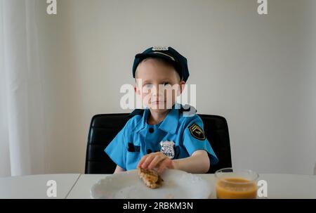 Ein Junge in schickem Kleid als Polizist, der Frühstück isst Stockfoto