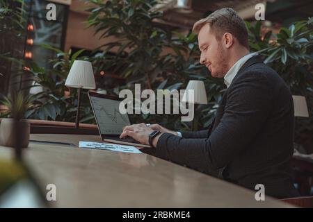 Fokussierter Geschäftsmann, der im Büro mit Dokumenten arbeitet und ein Notebook verwendet Stockfoto