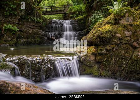 Die Sychryd Cascades oder Sgydau Sychryd Falls mit Holzbrücke im Waterfall Country in der Nähe von Dinas Rock, Pontnedfechan, Brecon Beacons National Park, South Wales, Großbritannien. Wasser mit langer Exposition. Stockfoto