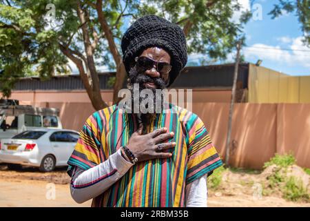 Glücklicher Rastafari in bunter Kleidung und Wollmütze, mit Dreadlocks und positiver Denkweise, Friedensring an seinem Finger Stockfoto