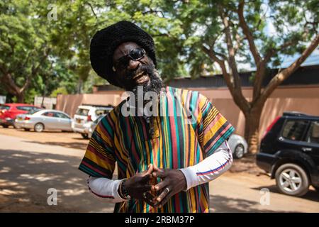 Glücklicher Rastafari in bunter Kleidung und Wollmütze, mit Dreadlocks und positiver Denkweise, Friedensring an seinem Finger Stockfoto