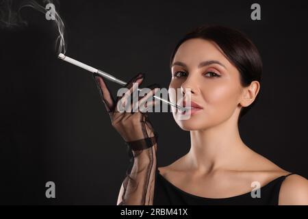 Frau mit langem Zigarettenhalter zum Rauchen auf schwarzem Hintergrund Stockfoto