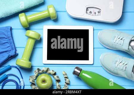 Tablet, Turnschuhe und Sportausrüstung auf hellblauem Holztisch, flach liegend. Persönliches Training Stockfoto