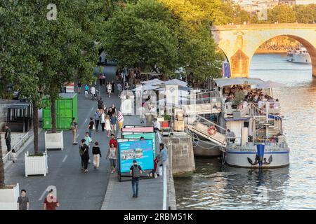 Die Leute spazieren im Abendlicht auf der seine, am rechten Ufer der Voie Georges Pompidou, mit Bootsbars und Restaurants gegenüber der Ile Saint-Louis. Paris. Stockfoto