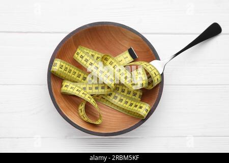 Schüssel mit Maßband und Gabel auf weißem Holztisch, flach liegend. Gewichtsverlust-Konzept Stockfoto