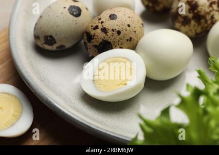 Ungeschälte und geschälte hart gekochte Wachteleier auf dem Teller, Nahaufnahme Stockfoto