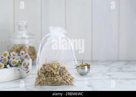 Duftbeutel mit getrockneten Kamillenblumen auf weißem Marmortisch, Platz für Text Stockfoto