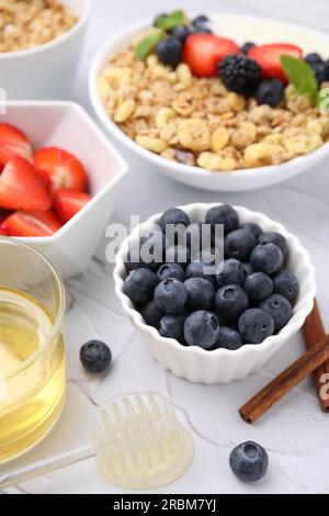 Frische Beeren, Haferflocken und Honig auf weißem Tisch, Nahaufnahme. Gesundes Frühstück Stockfoto