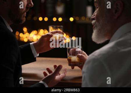 Männer mit Whiskey-Gläsern, die sich an einem Holztisch in der Bar unterhalten Stockfoto