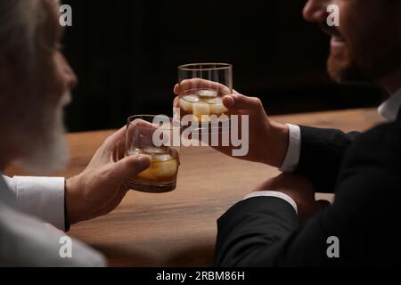 Männer mit Whiskey-Gläsern, die sich an einem Holztisch in der Bar unterhalten Stockfoto