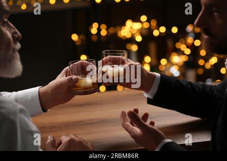 Männer mit Whiskey-Gläsern, die sich an einem Holztisch in der Bar unterhalten Stockfoto