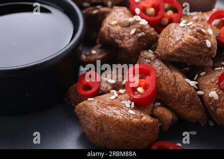 Leckere Sojasoße, geröstetes Fleisch mit Chili-Pfeffer und Sesam auf dunklem Teller, Nahaufnahme Stockfoto