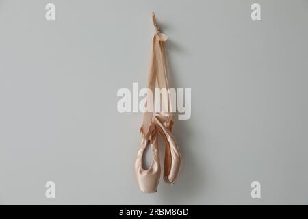 Wunderschöne beige Ballettschuhe mit niedlichen Bändern, die an hellgrauen Wänden hängen Stockfoto