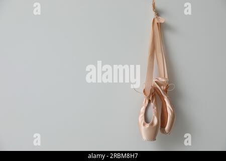 Wunderschöne beige Ballettschuhe mit niedlichen Bändern, die an hellgrauen Wänden hängen. Platz für Text Stockfoto