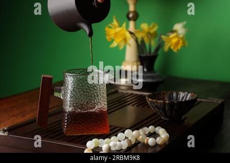 Frisch gebrühten pu-erh-Tee in den Krug auf dem Holztisch gießen Stockfoto