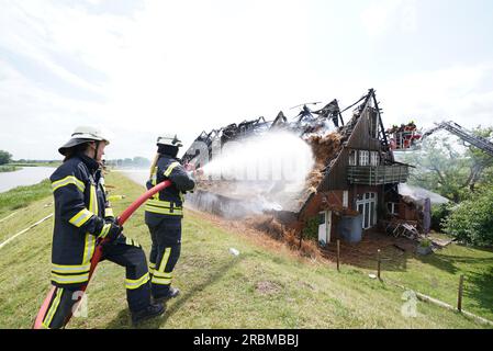 Moorrege, Deutschland. 10. Juli 2023. Feuerwehrleute löschen ein brennendes strohgedecktes Haus. Am Montag brannte ein Strohhaus in Moorrege im Pinneberg-Bezirk. Die Ursache des Feuers ist noch unklar, sagte eine Polizeisprecherin. Es ist möglich, dass ein Blitzschlag das Feuer im strohgedeckten Haus verursacht hat. Die Menschen waren Berichten zufolge nicht in Gefahr. Kredit: Marcus Brandt/dpa/Alamy Live News Stockfoto