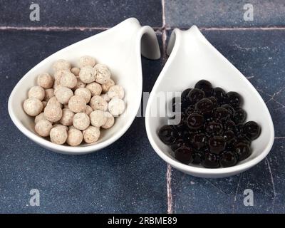 Rohe und gekochte Tapiokugeln mit verschiedenen Geschmacksrichtungen, auch bekannt als boba in Seifenblasentee, auf grauem Fliesenhintergrund. Eine Zutat für Perlmutttee. Stockfoto