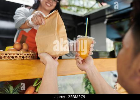 Ein Mann, der eine Bestellung und ein alkoholfreies Getränk von einem Food-Truck-Arbeiter annimmt Stockfoto