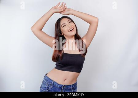 Porträt einer glücklichen jungen Asiatin, die ein Crop Top trägt, isoliert auf weißem Hintergrund. Diätkonzept. Stockfoto