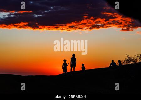 Schatten und Silhouetten von Menschen, die den Sonnenuntergang auf dem Berg Spitzkuppe in Namibia, Afrika, beobachten Stockfoto