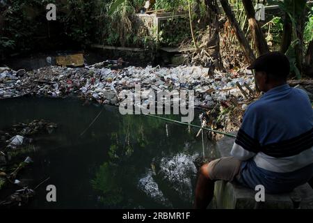 Bantul, Yogyakarta, Indonesien. 10. Juli 2023. Ein Mann fischt in der Nähe von Müll, der auf der Oberfläche eines Flusses in Bantul, Yogyakarta, schwimmt. (Kreditbild: © Angga Budhiyanto/ZUMA Press Wire) NUR REDAKTIONELLE VERWENDUNG! Nicht für den kommerziellen GEBRAUCH! Stockfoto