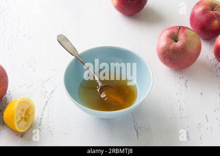 Eine Schüssel Honig und Zitronensaft, umgeben von frischen Äpfeln auf hellblauem Hintergrund. Stufe der Zubereitung von köstlichem Obstkuchen oder anderem Dessert Stockfoto
