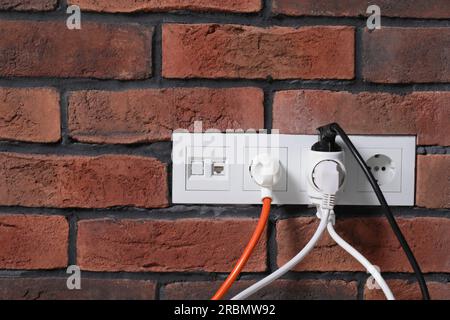 Viele verschiedene elektrische Netzstecker in Steckdosen an roter Backsteinwand, Platz für Text Stockfoto