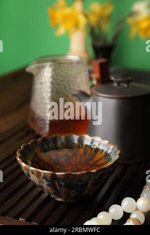 Tasse mit frisch gebrühtem pu-erh-Tee und Gebetsperlen auf Holztablett, Nahaufnahme Stockfoto