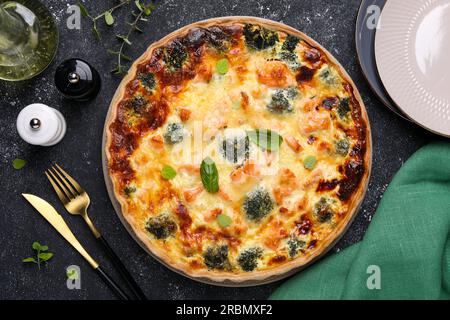 Köstliche hausgemachte Lachs-Quiche mit Brokkoli auf schwarzem Tisch, flach liegend Stockfoto