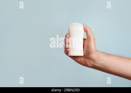 Männliche Hand hält weißes Deodorant auf blauem Hintergrund. Nahaufnahme. Speicherplatz kopieren Stockfoto