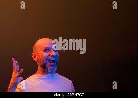 Ein glücklicher Mann mit kahlem Bart, der lustige Gesten macht. Konzept von Stärke, Leistung und Erfolg. Isoliert auf dunkelrotem Hintergrund. Stockfoto