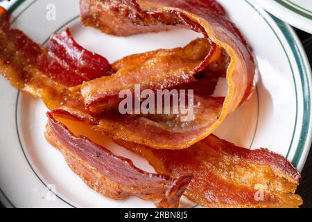 Nahaufnahme von knusprigem gebratenem Speck auf weißem Teller, amerikanisches Frühstück von oben Stockfoto